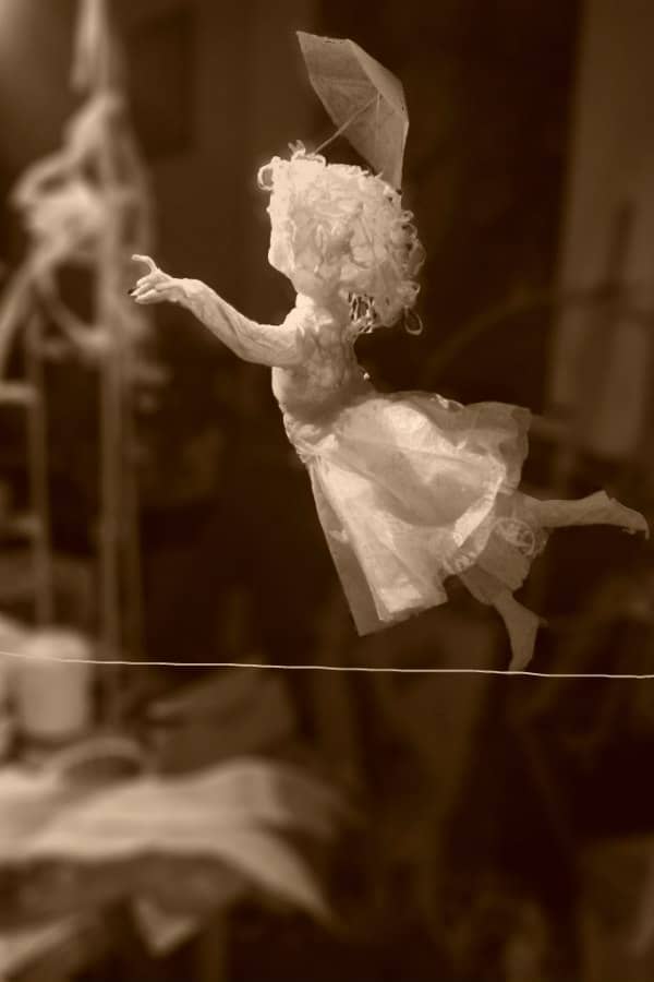 all-white paper sculpture of young girl walking on tightrope with one arm outstretched